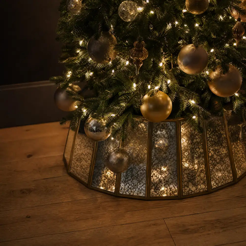 A close view of the antiqued mirrored collar at the foot of the tree, the lights above it repeated in the metal.