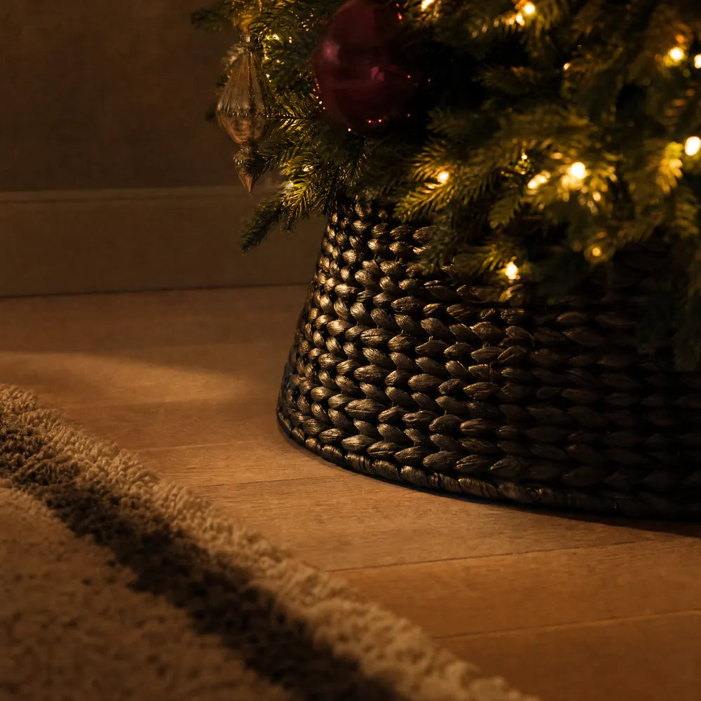 A dark brown basket-weave collar around the foot of the tree, low light raking across the weave.